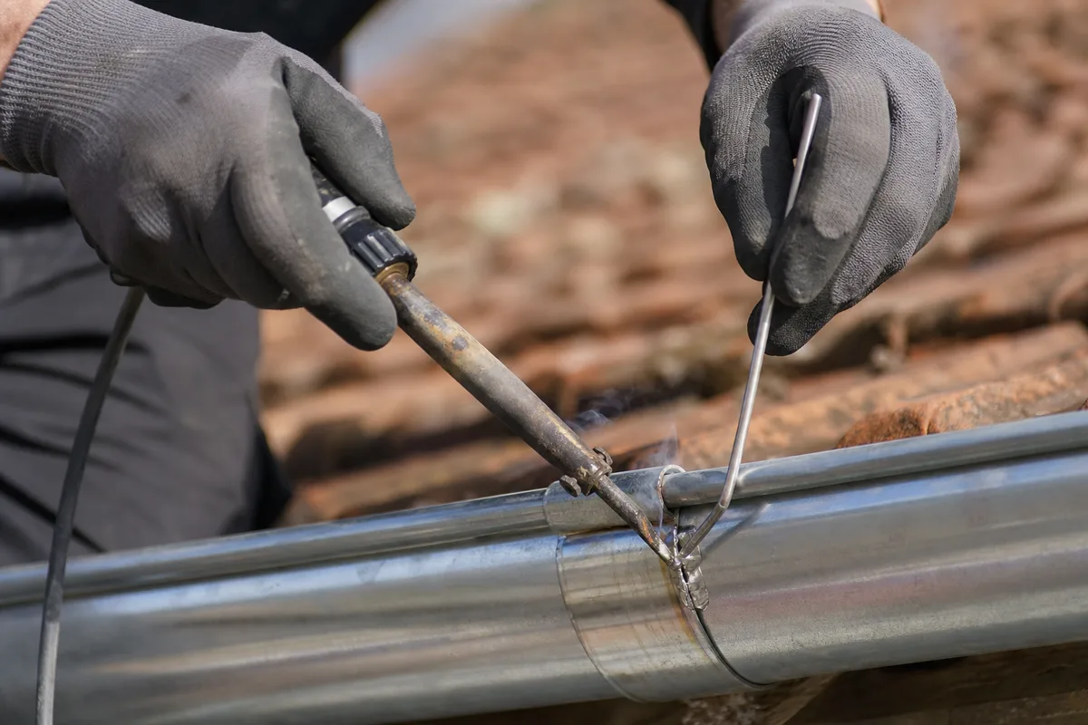 Mains d’un couvreur ressoudant à l’étain la jonction d’une gouttière en zinc